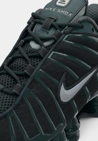 Μαύρα αθλητικά παπούτσια Nike Shox με πλέγμα υφής, πράσινες λεπτομέρειες και ασημένιο λογότυπο Nike. Εντυπωσιακή αμ cushioning με τακούνι και σύστημα δέσιμο.