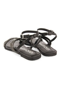 Sandalias planas negras con tiras trenzadas, cuentas decorativas y cierre de hebilla. Suela texturizada con marca en la plantilla.