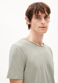 Hellgrünes T-Shirt mit kurzen Ärmeln und Rundhalsausschnitt, aus weichem Stoff, mit glatter Textur und dezenten Nähten entlang der Kanten.