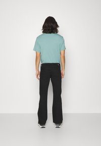 Ljus teal kortärmad t-shirt kombinerad med svarta utställda jeans. Synlig sömnad och fickor på jeansen, sportskor med flerfärgade accenter.