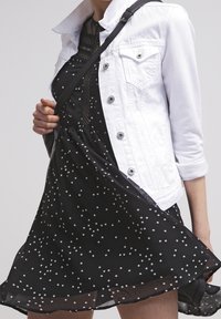 Veste en denim blanche avec des boutons en argent sur une robe noire dotée d'un tissu translucide et de motifs géométriques blancs dispersés.
