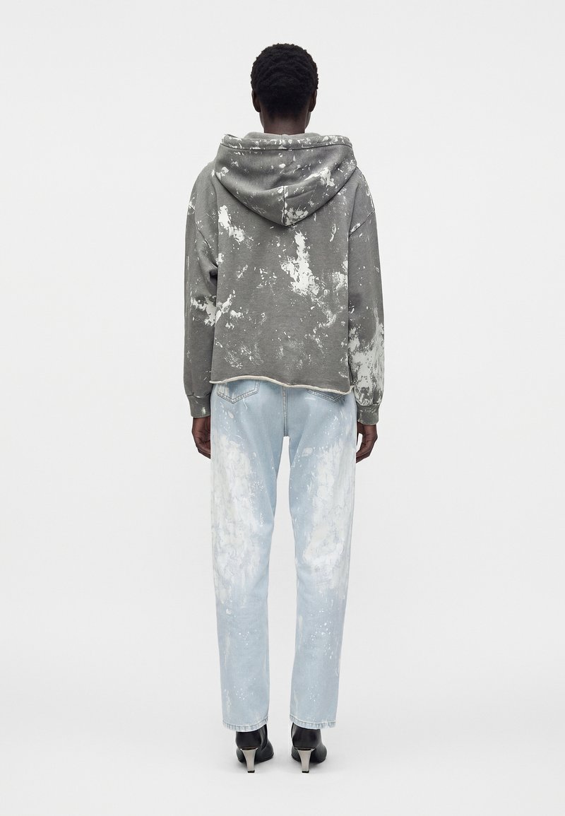 Person wearing gray and white paint-splattered hoodie and light blue jeans with similar paint splatters, standing with back to the camera.