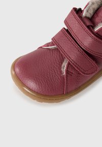 Zapato de cuero burdeos con dos correas de Velcro, superficie texturizada, interior acolchado y suela de goma. Presenta sutiles acentos en la costura.
