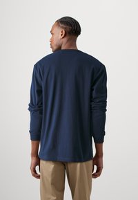 Marineblå langermet skjorte laget av bomull, med rund hals og ribbestrikkede mansjetter. Glatt tekstur, avslappet passform og minimalistisk design.