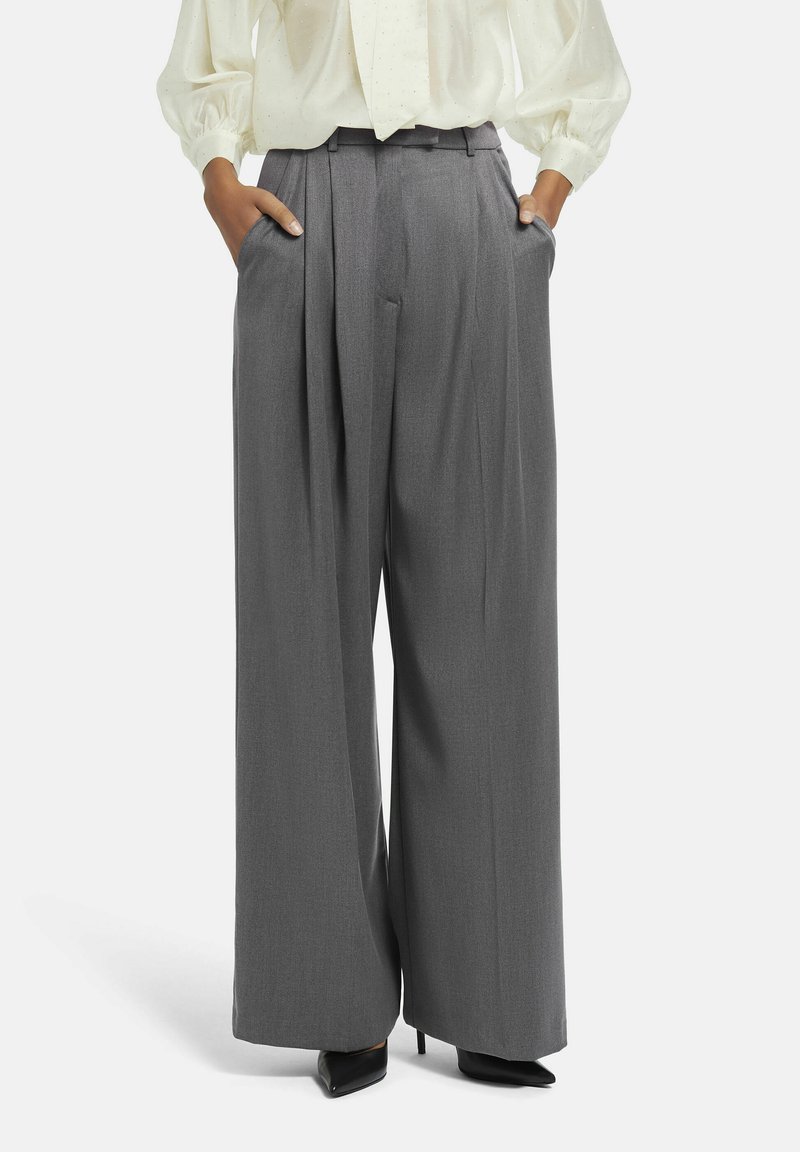 Pantalons gris à jambes larges avec un devant plissé, en tissu texturé ; dotés de poches latérales et d'une taille haute. Associés à un chemisier léger.