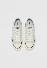 Šviesiai mėlyni kanvoso sportbačiai su baltais raišteliais, juodu apvadu ir guminiu priekiu. Ant liežuvėlio yra „Converse All Star“ etiketė.