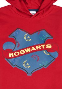 Rode sweatshirt met capuchon, voorzien van een blauw schildontwerp met het woord "HOGWARTS" in goud. Zeven huisnamen in kleurrijke tekst omringen het schild.