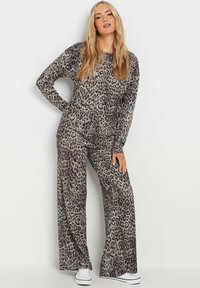 Completo lounge con stampa leopardata realizzato in morbido tessuto. Top a maniche lunghe e pantaloni a gamba larga in tonalità di grigio e nero, abbinati a sneaker bianche.
