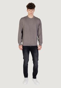 Pull en tricot gris avec un motif en losanges, col rond et poignets côtelés, associé à un jean foncé et des baskets blanches.