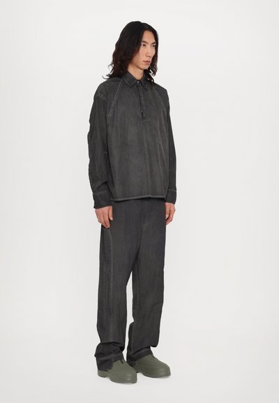 Chemise à col boutonné, à manches longues, de couleur gris foncé, associée à un pantalon ample assorti et des chaussures vertes à enfiler.