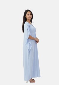 Lys blå maxikjole med brede ærmer, tekstureret stof og strammet talje. Klare, flade sandaler fuldender outfittet.