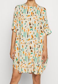 Robe à manches courtes en tissu beige arborant un motif abstrait de formes orange, vertes et noires ; coupe ample avec un col rond et une fermeture à boutons.