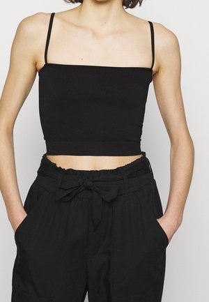 Czarny prążkowany crop top z cienkimi regulowanymi ramiączkami, o prostym dekolcie i dopasowanym kroju. Noszony z czarnymi spodniami o wysokim stanie.