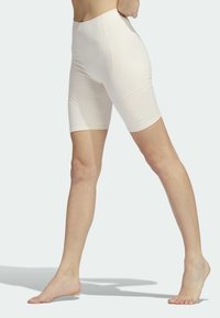 Světlé béžové cyklistické šortky s vysokým pasem a hladkou strukturou, které mají přiléhavý střih a diskrétní švy. Logo na dolní části nohavice.