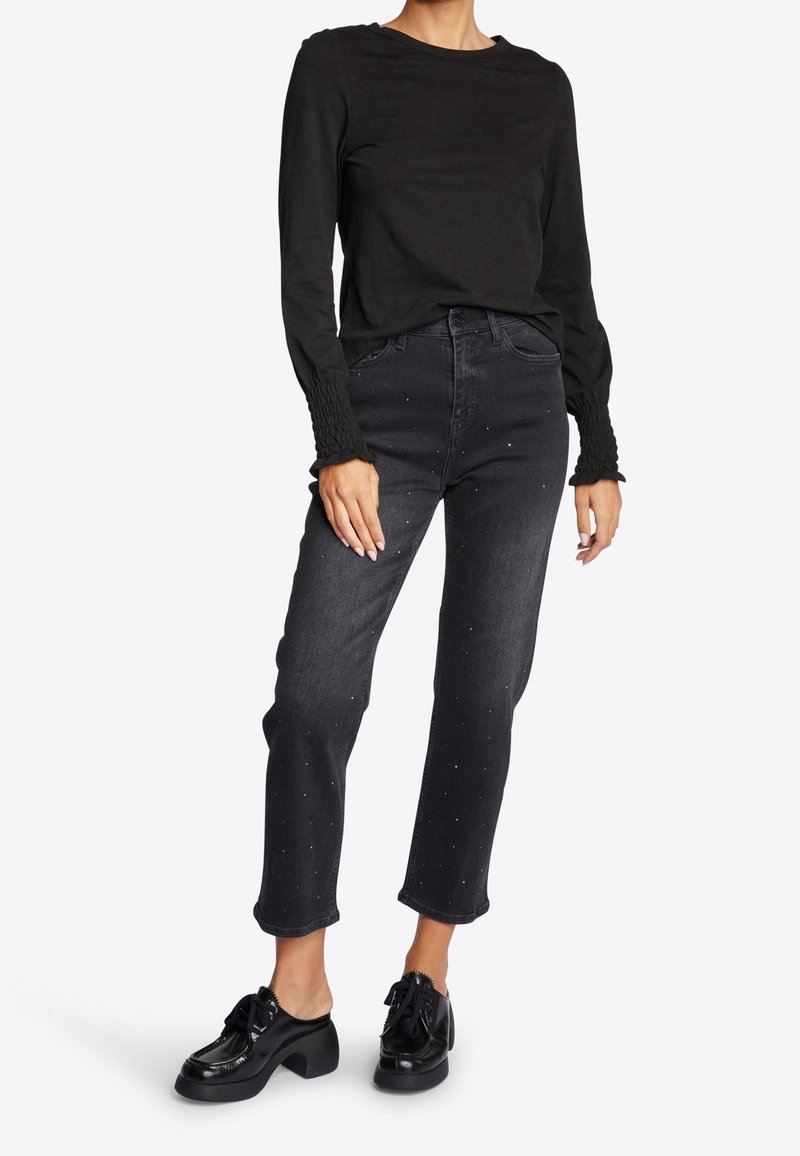 Maglietta nera a maniche lunghe con maniche testurizzate, abbinata a jeans scuri a vita alta con borchie argentate e scarpe platform nere.