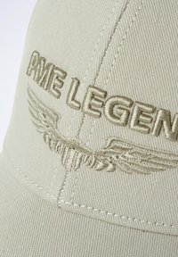 Casquette beige avec broderie en relief "PME LEGEND" et design d'ailes, présentant une texture douce et des détails de couture visibles.