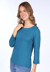 Tee in Türkis mit 3/4-Ärmeln, aus weichem Stoff gefertigt, mit Rundhalsausschnitt, glatter Textur und lässiger Passform, kombiniert mit blauen Jeans.