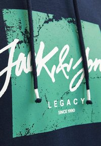 Marine hoodie met een gestructureerde groene grafiek en witte bedrukking "Jack & Jones LEGACY sinds 1990" en zwarte koorden met witte uiteinden.