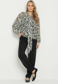 Przezroczysta, długosleeve bluzka w czarno-białym zwierzęcym wzorze z wiązaniem w talii, w połączeniu z czarnymi spodniami i czarnymi balerinami.
