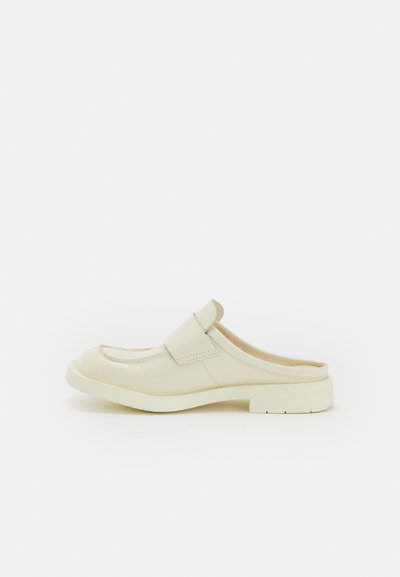 Beige läder slip-on sko med rund tå, platt sula och ett dekorativt sömmönster. Har ett justerbart band på ovandelen.