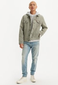 Chaqueta de mezclilla gris claro sobre una sudadera gris, combinada con jeans azul claro y zapatillas blancas. Corte estándar con dos bolsillos frontales.