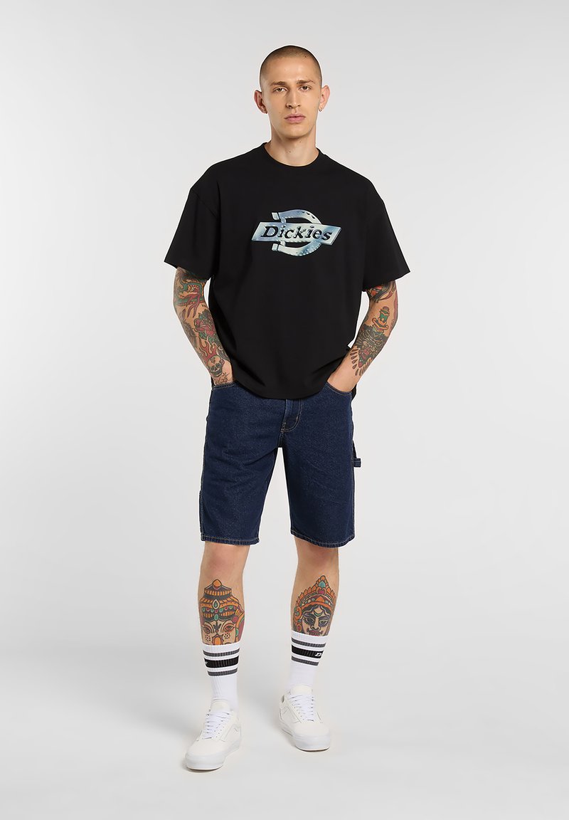 Black short-sleeve t-shirt with a blue graphic logo, paired with blue denim shorts and white sneakers, featuring striped white and black socks.