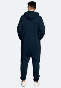 Marineblauer Kapuzenanzug aus weichem Stoff, mit entspanntem Schnitt, elastischen Bündchen und einer Kängurutasche, getragen mit weißen Sneakern.