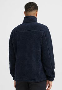 Navy blue fleece jacket with a high collar, textured surface, and a relaxed fit. No visible fasteners or pockets on the backside.