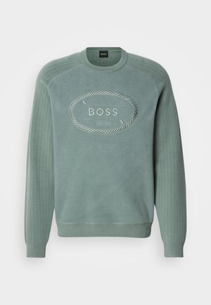 Grønn sweatshirts med en teksturert overflate, ribbede sidepaneler og et preget logo i oval form på forsiden.