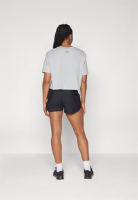 Camiseta gris corta con cuello redondo y logo en la espalda, combinada con pantalones cortos deportivos negros y zapatillas negras. Diseño minimalista.