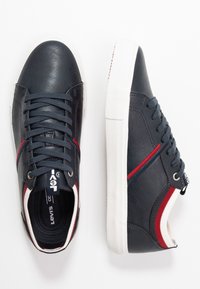 Baskets en cuir bleu marine avec semelles en caoutchouc blanches, ornées d'accents rouges et bleus, bout rond, et design standard à lacets.