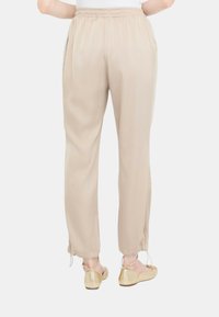Pantaloni beige da donna realizzati in materiale leggero, con vita elastica e orli legati, abbinati a scarpe flat dorate.