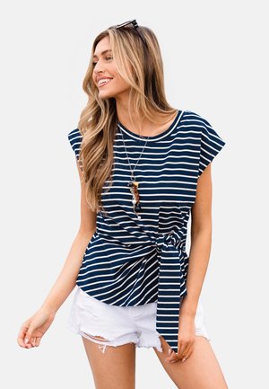 Granatowo-biały top w paski z krótkimi rękawami, okrągłym dekoltem i wiązaniem z przodu. Połączony z postrzępionymi białymi szortami.