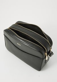 Black leather bag with two zippered compartments and gold hardware. Smooth texture with a structured rectangular shape and embossed logo.