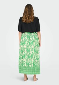 Top nero a maniche corte, gonna lunga verde con motivo floreale su sfondo crema e orlo decorato. Tessuto liscio e vestibilità comoda.