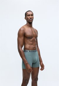 Zelene pamučne bokserice s crnim pojasom na kojem se nalazi logo "BJÖRN BORG", strukturirani kroj, glatka tekstura i minimalistički dizajn.