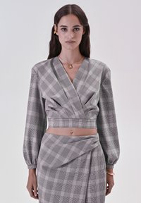 Blusa cropped a quadri grigi e neri con scollatura a V e maniche a sbuffo, abbinata a una gonna coordinata con pieghe e un accento drappeggiato.