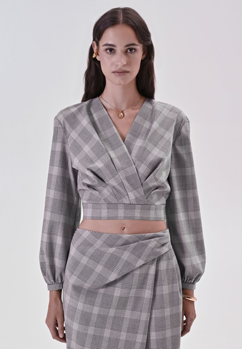 Blusa cropped a quadri grigi e neri con scollatura a V e maniche a sbuffo, abbinata a una gonna coordinata con pieghe e un accento drappeggiato.