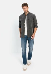Gray button-up shirt with two chest pockets, white t-shirt underneath, blue denim jeans, and beige sneakers. Model stands facing forward.