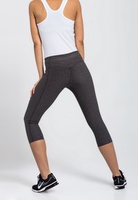 Leggings gris longueur cheville avec une taille haute, fabriqués en tissu texturé, associés à des chaussures de sport noires et un débardeur blanc.