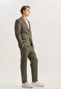 Traje gris de dos piezas con tejido texturizado, blazer de un botón, pantalones ajustados, combinado con zapatillas blancas y una camiseta blanca.