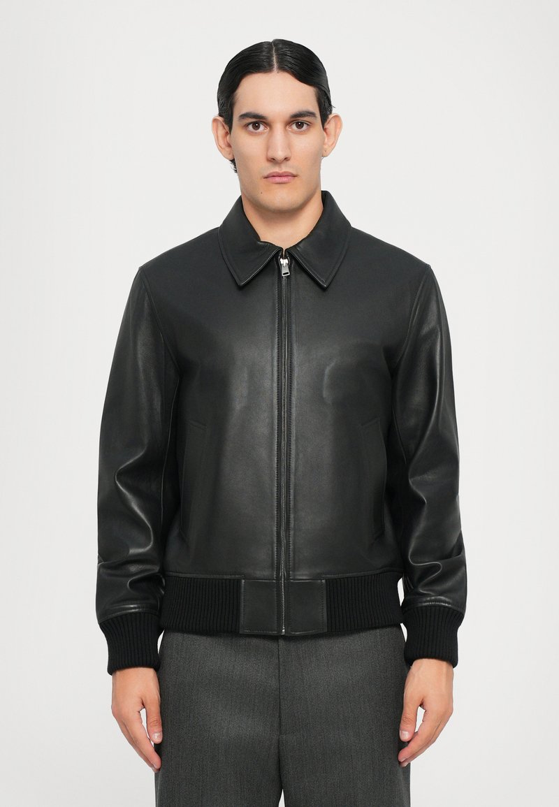 Veste bomber en cuir noir avec fermeture éclair à l'avant, large col et poignets et ourlet côtelés. Texture lisse et coupe ajustée.