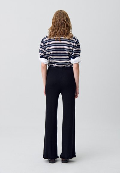 Pantalones acampanados de canalé negros con dobladillos de volantes, combinados con una camisa de rayas de corte oversized con mangas remangadas.