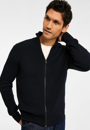 Marinblå ribbat stickad zip-tröja med hög krage, långa ärmar och dragkedjestängning. Matchad med blå denim-jeans.