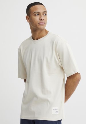 Beige bomull t-skjorte med korte ermer, rund hals og rett snitt. Har en liten merkeadresse på den nederste siden. Glatt tekstur.