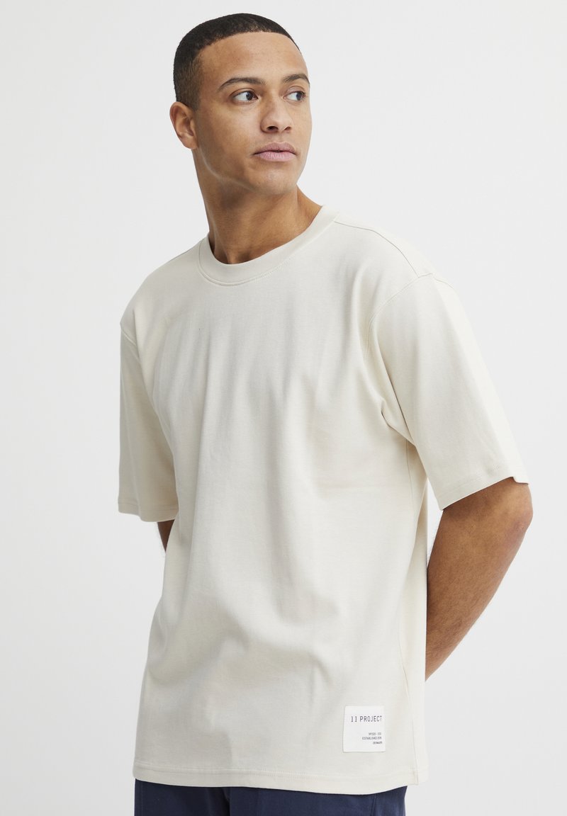 Beige bomull t-skjorte med korte ermer, rund hals og rett snitt. Har en liten merkeadresse på den nederste siden. Glatt tekstur.