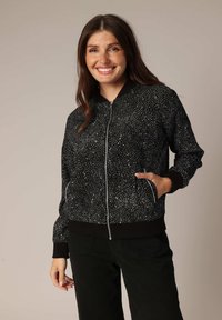 Zwarte bomberjack met witte spikkels, ribbelboorden en onderrand, ritssluiting en zijzakken. Zachte textuur met een casual pasvorm.