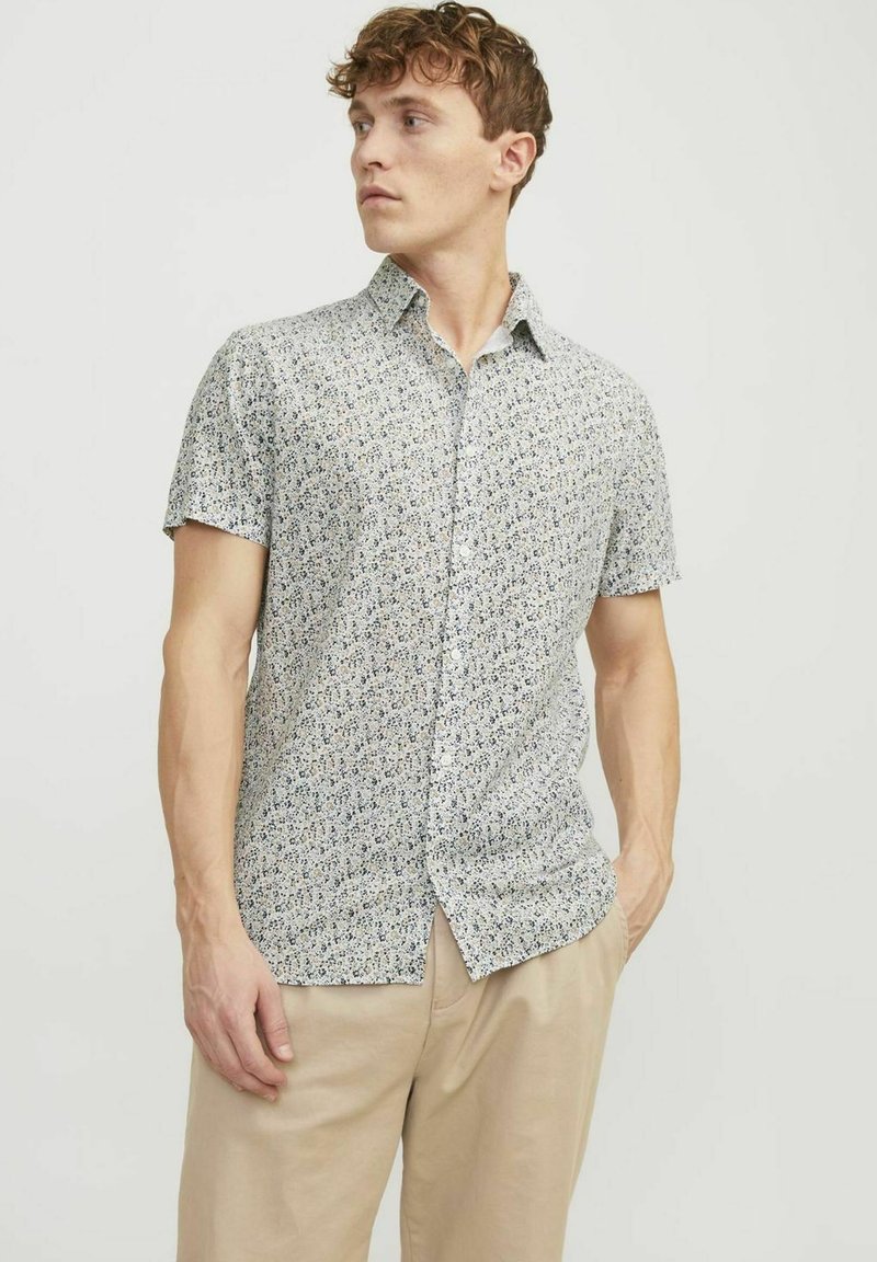 Camicia a maniche corte con bottoni in tessuto leggero, con un motivo floreale in tonalità di blu e bianco. Taglio dritto, colletto standard e vestibilità rilassata.