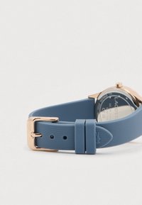 Blue ribbed silicone watch strap with rose gold buckle and loops, partially showing stainless steel watch case back.