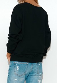 Černá mikina s širokým výstřihem, spadlými rameny a dlouhými rukávy, v kombinaci se světle modrými zničenými džíny. Jednoduchý design, volný střih.